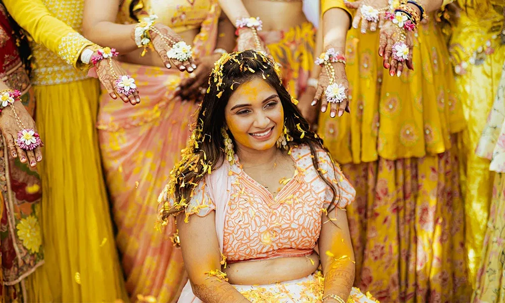 Braut wird bei einer Haldi-Zeremonie mit Kurkuma und Blüten bestreut.