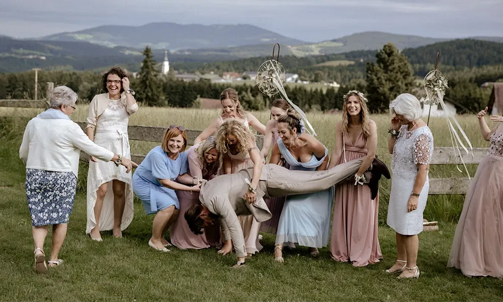 Brautjungfern und Familie heben den Bräutigam spielerisch in die Luft.