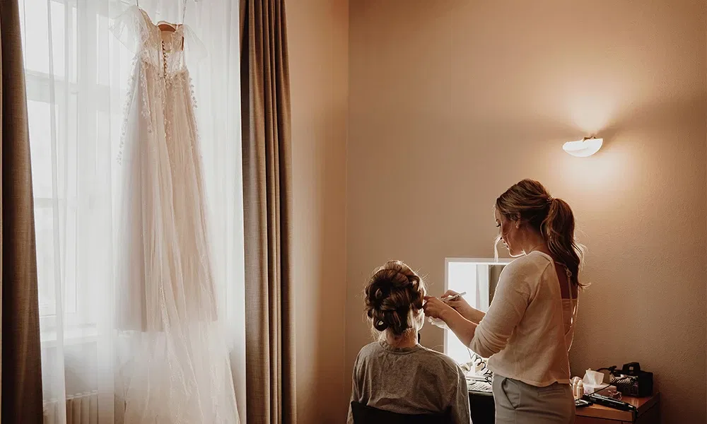 Getting-Ready-Moment mit Stylistin, während das Brautkleid bereit hängt.