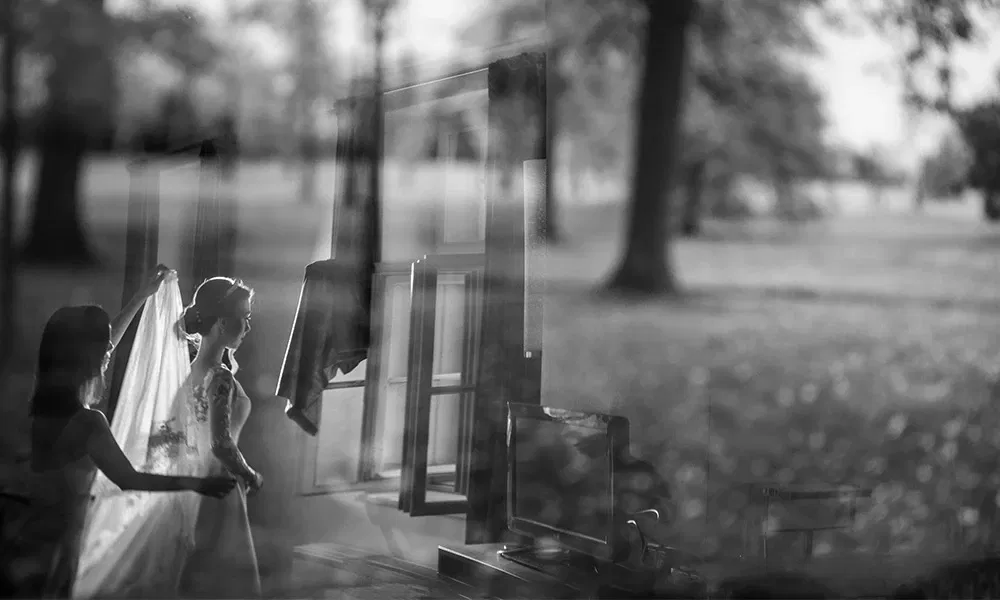 Künstlerische Spiegelung einer Braut mit Begleitung beim Fenster.