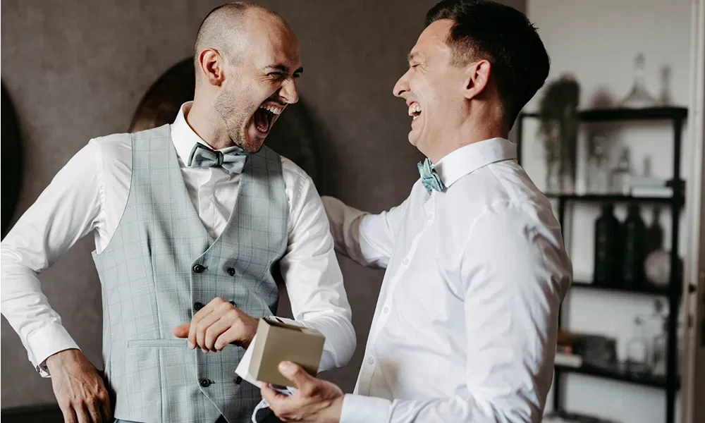 Zwei Freunde lachen ausgelassen beim Ankleiden für die Hochzeit.