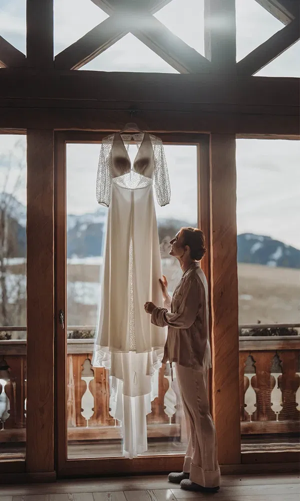 Braut bewundert ihr Kleid im Morgenlicht vor alpiner Kulisse.
