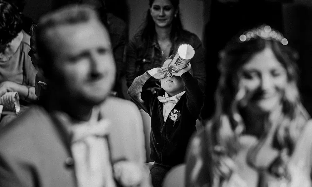 Kind trinkt genüsslich aus einer Dose während der Zeremonie – Fokus auf Alltag im Hochzeitstrubel.