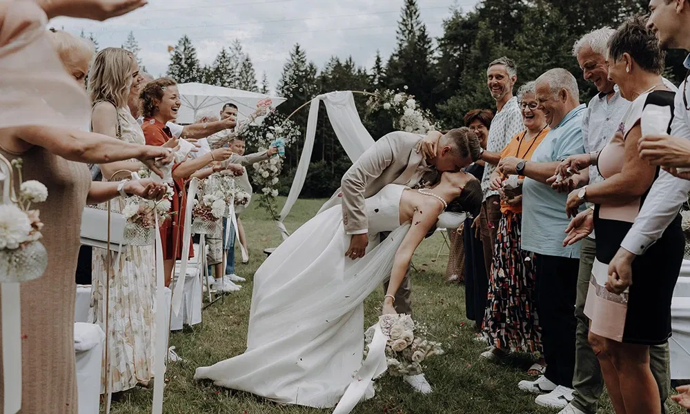 Das Brautpaar küsst sich innig, während Gäste im Spalier Seifenblasen pusten.