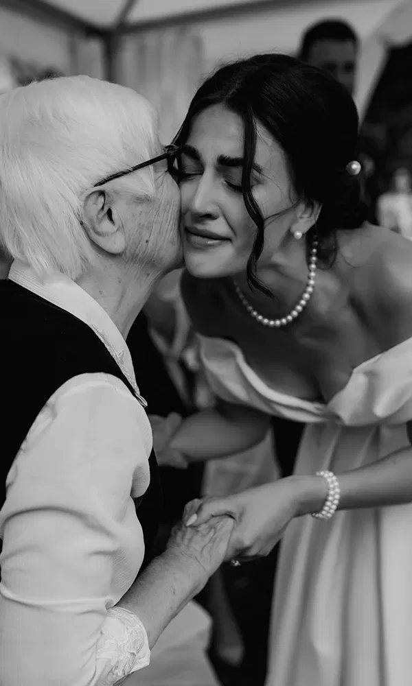 Die Braut bekommt liebevoll einen Kuss von ihrer Großmutter und hält dabei ihre Hände.
