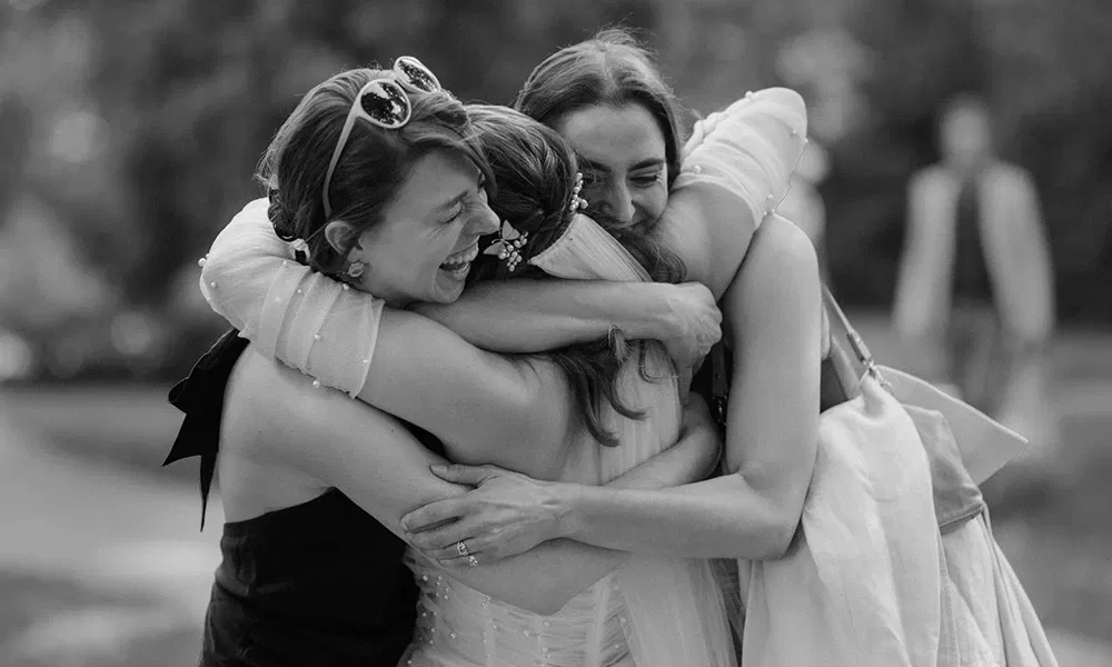 Drei Freundinnen umarmen sich voller Freude und Rührung beim Wiedersehen auf der Hochzeit.