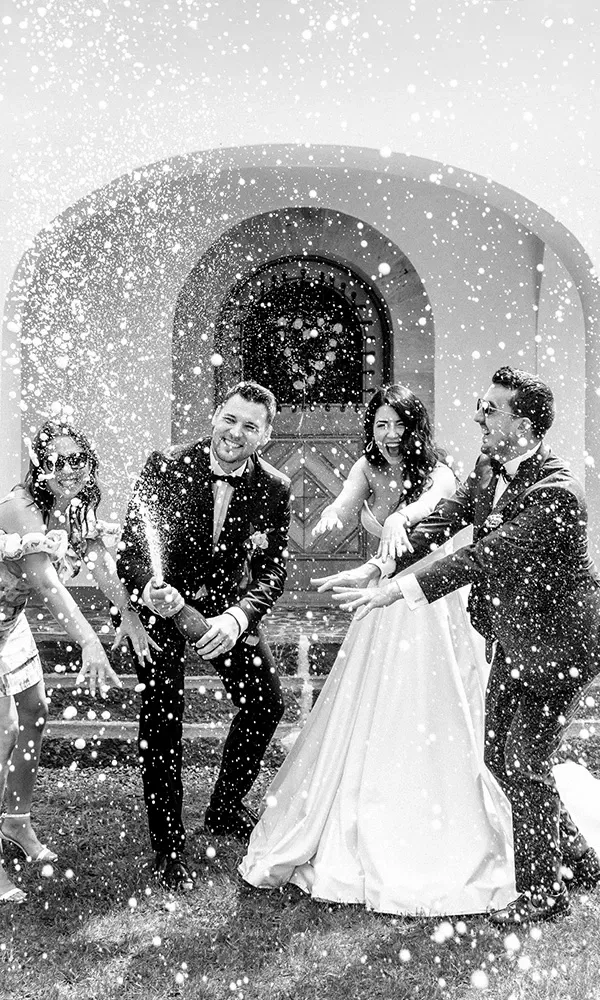 Das Brautpaar und Gäste feiern ausgelassen mit einer spritzenden Champagnerflasche.