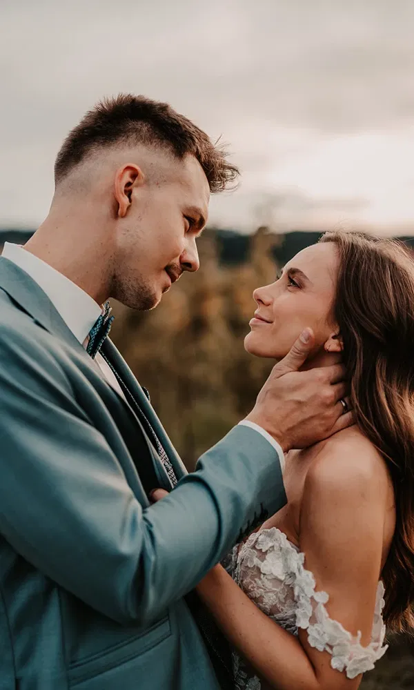 Brautpaar in innigem Moment bei Sonnenuntergang, verliebter Blick und zarte Berührung.