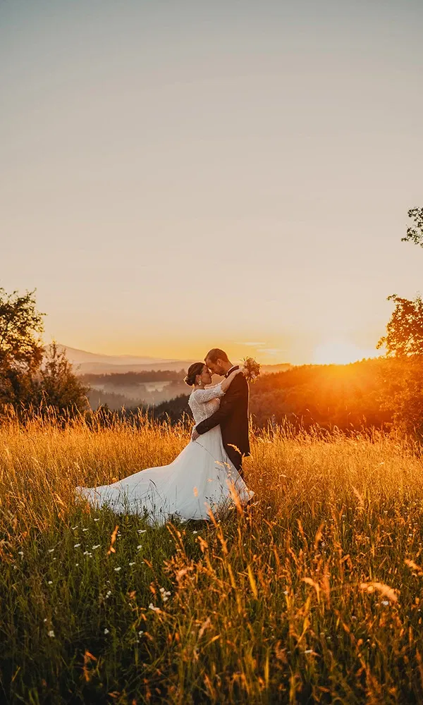 Braut und Bräutigam in einer goldenen Wiese bei Sonnenuntergang, fest umarmt.