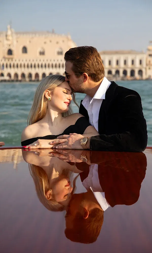 Paar auf Boot in Venedig, zärtlicher Kuss auf die Stirn mit Spiegelung im Holz.