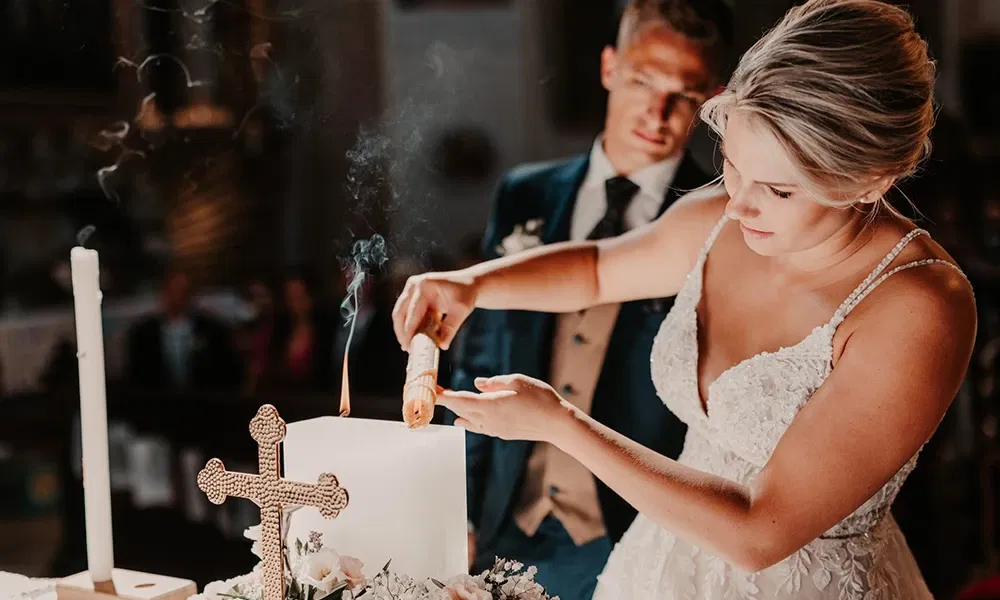 Braut zündet feierlich die Hochzeitskerze in der Kirche an, während der Bräutigam sie liebevoll beobachtet.
