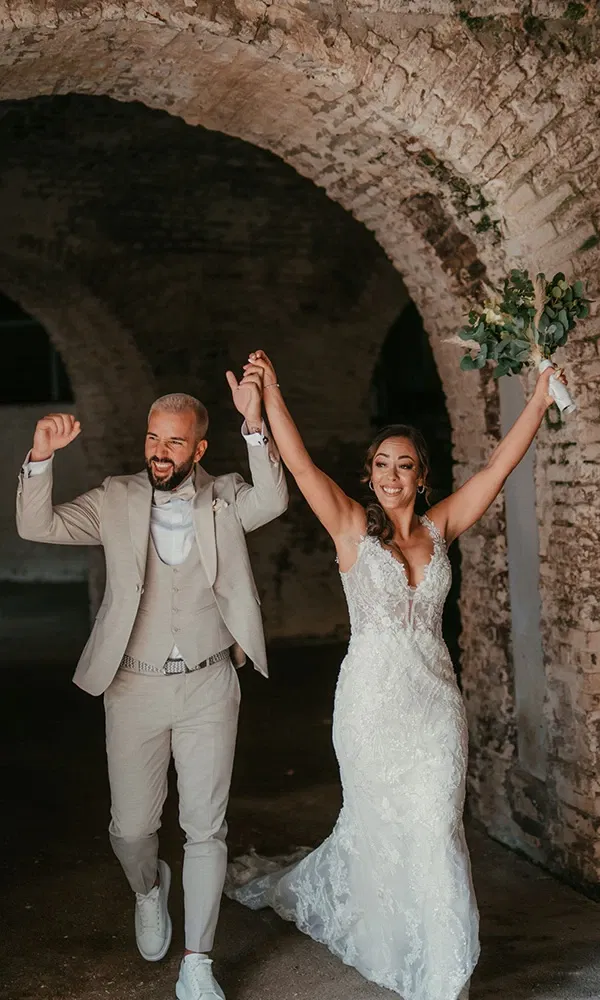 Frisch verheiratetes Paar verlässt strahlend die Zeremonie und jubelt mit erhobenen Armen.