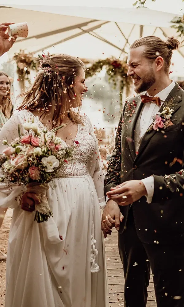 Braut und Bräutigam lächeln sich verliebt an, während sie unter einem Konfettiregen schreiten.