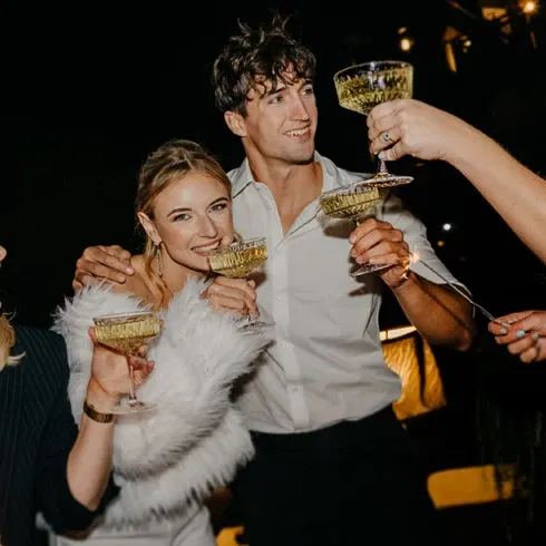 Hochzeitsgäste stoßen fröhlich mit Sektgläsern bei Nacht an.