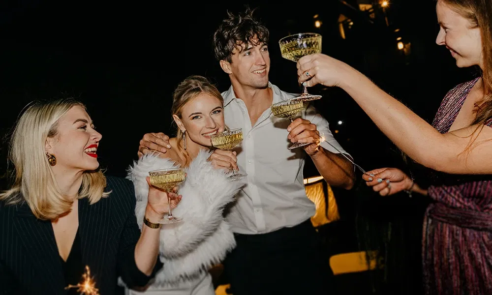 Hochzeitsgäste stoßen fröhlich mit Sektgläsern bei Nacht an.