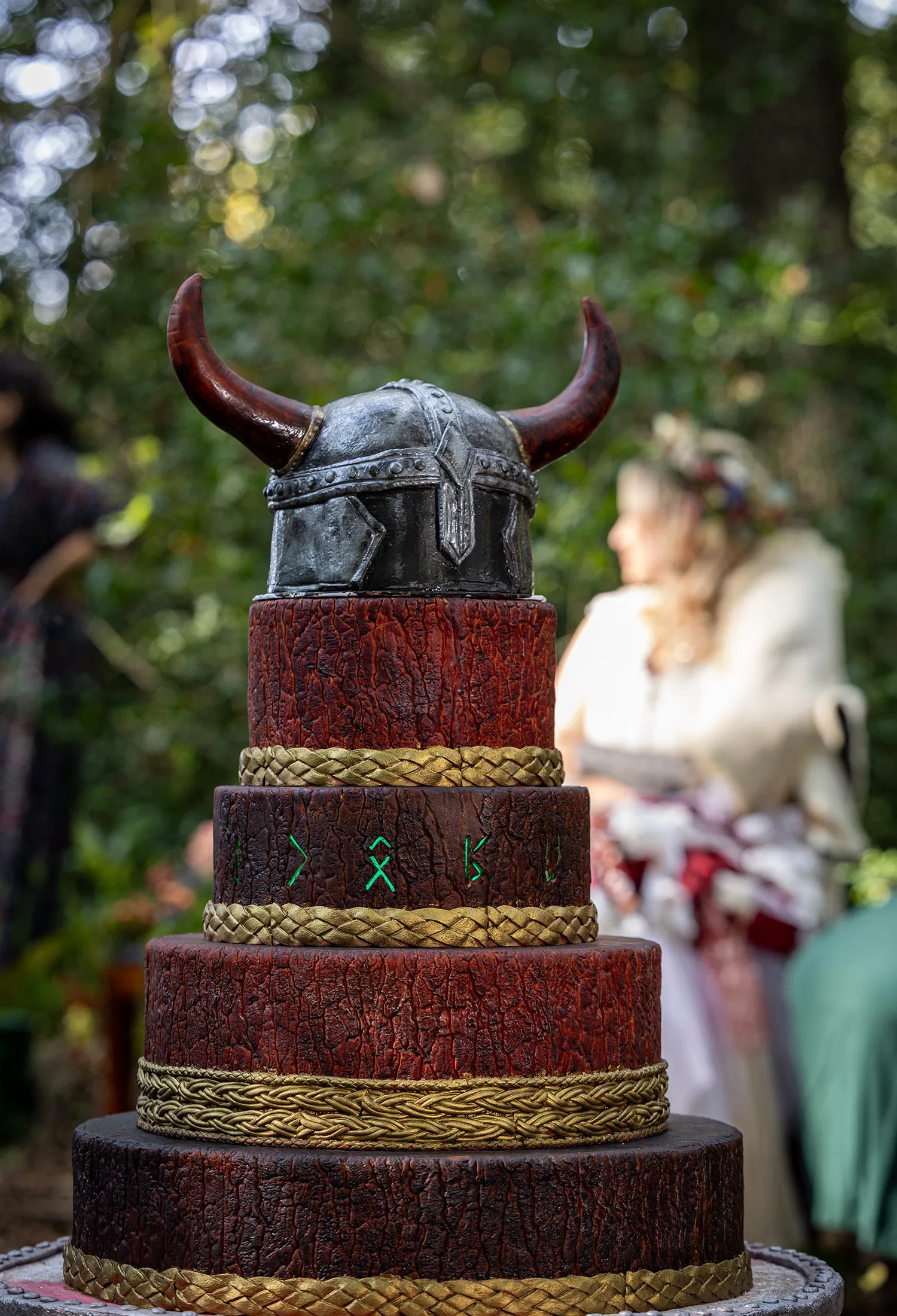 Wikinger Hochzeitstorte mit rustikaler Holzoptik, goldenen Flechtdetails und Wikingerhelm als Tortenaufsatz im Wald