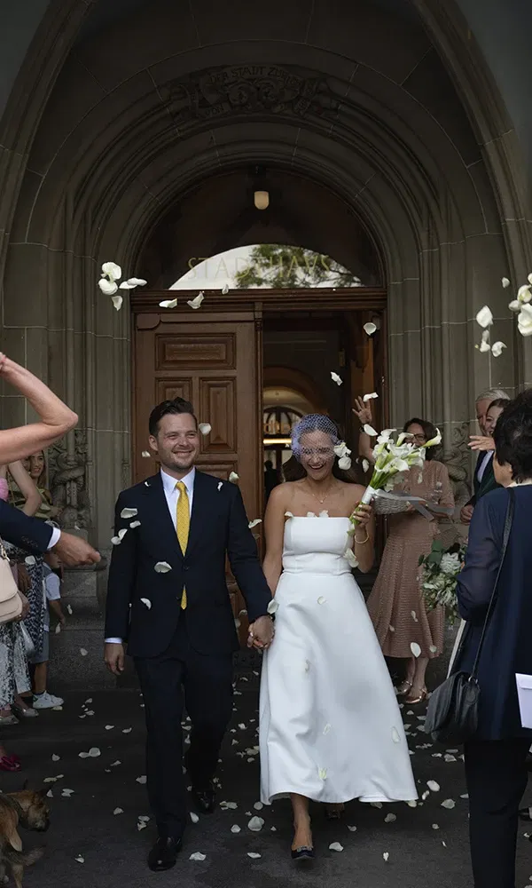 Frisch verheiratetes Paar verlässt das Standesamt in Zürich unter einem Blütenregen und strahlenden Gesichtern.