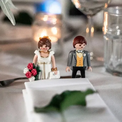 Zwei Playmobil-Figuren als Braut und Bräutigam stehen dekorativ auf einer festlich gedeckten Hochzeitstafel.