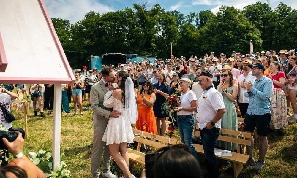 Festival-Hochzeit mit Publikum: Ein Brautpaar küsst sich nach der Zeremonie, umgeben von jubelnden Gästen auf dem Happiness Festival.