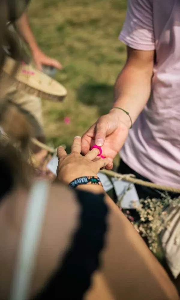 Nahaufnahme: Ein Festivalbesucher steckt einer anderen Person einen pinken Ring an den Finger.