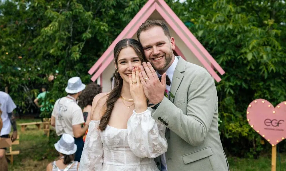 Frisch vermähltes Paar zeigt lachend seine Ringe vor der pinken Happy Chapel beim Happiness Festival.