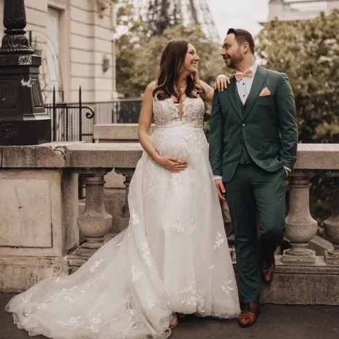 Schwangere Braut in weißem Kleid und ihr Bräutigam im grünen Anzug beim After-Wedding-Shooting in Paris mit Blick auf den Eiffelturm.
