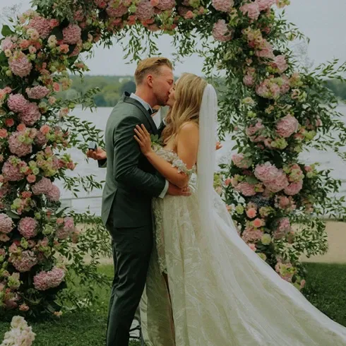 Das Brautpaar küsst sich nach der Trauung unter einem üppigen Blumenbogen.