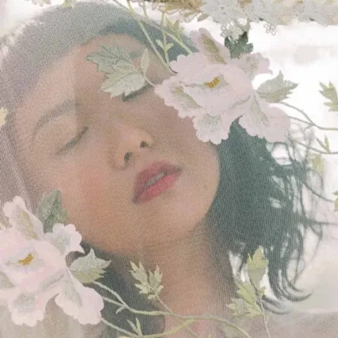 Frau mit geschlossenen Augen hinter einem bestickten Schleier mit floralen Motiven – verträumt und romantisch.