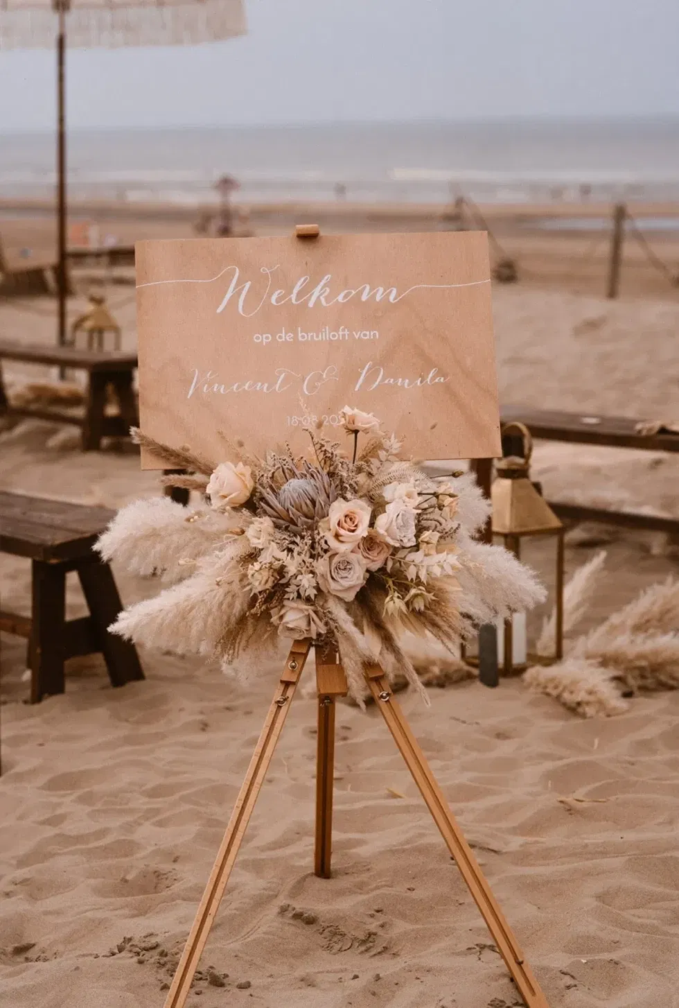 Holzschild mit Blumenstrauß auf Staffelei am Strand bei der Trauzeremonie