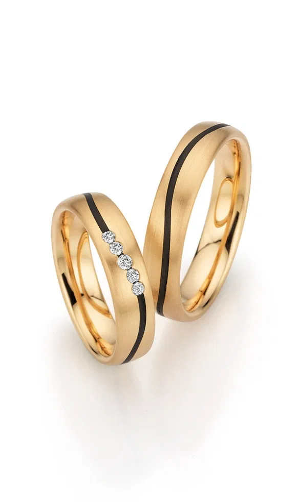 Goldene Trauringe mit matter Oberfläche und markanter schwarzer Carbonlinie, der schmalere Ring ist mit mehreren kleinen Diamanten verziert.