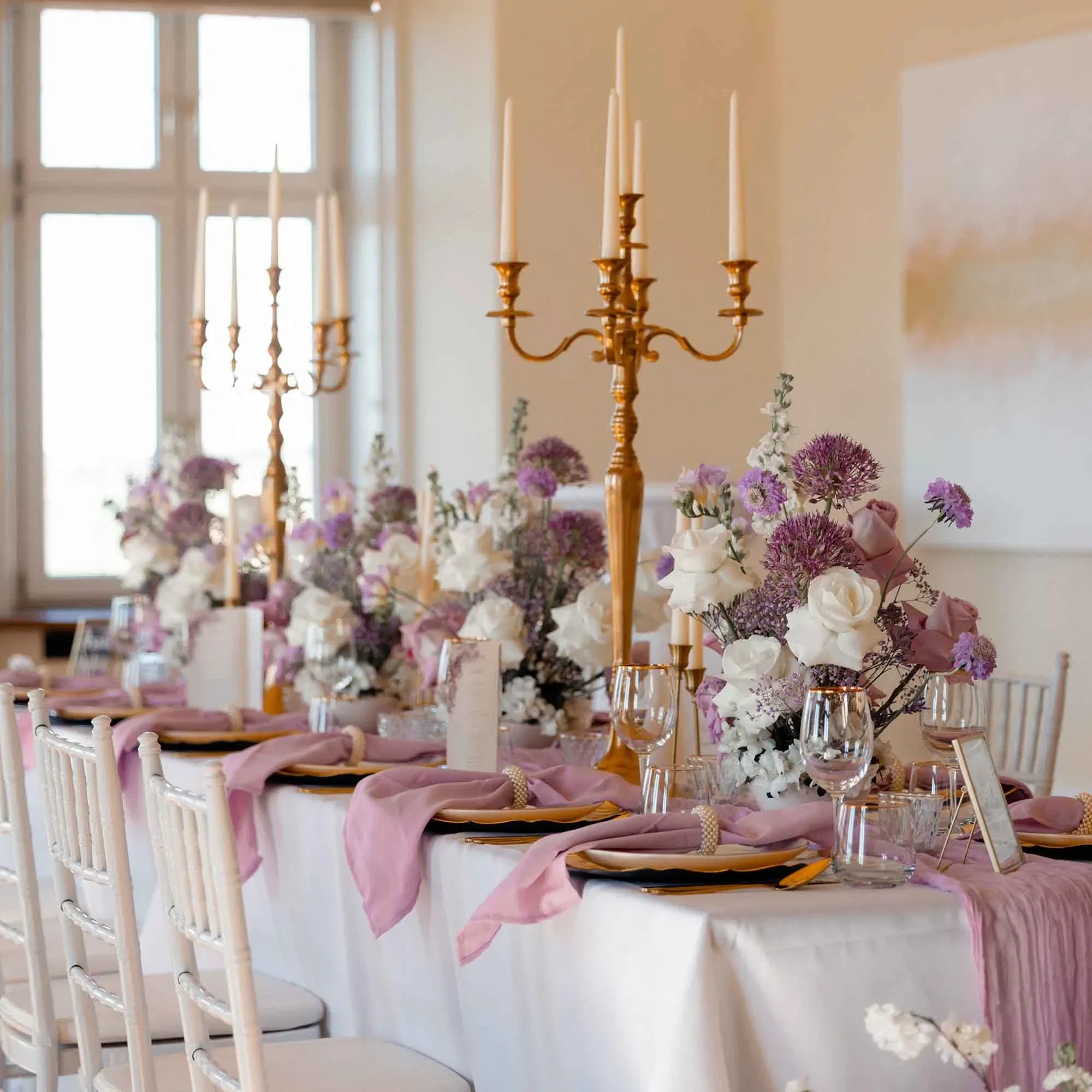 Festlich gedeckter Hochzeitstisch mit lila Blumengestecken, goldenen Kerzenleuchtern und eleganter Tischdeko