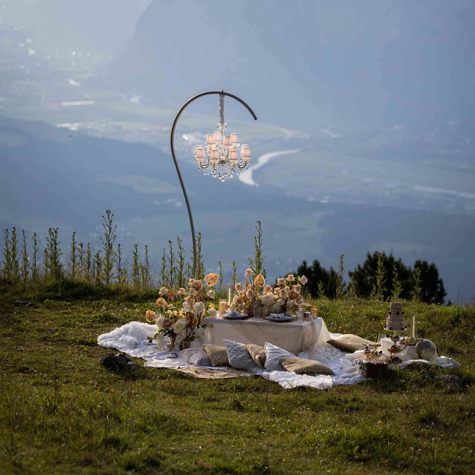 Luxus-Picknick in den Alpen mit elegant gedecktem Tisch, Blumenarrangement und Kronleuchter unter freiem Himmel.