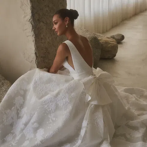 Modernes Casablanca Hochzeitskleid mit tiefem Rückendekolleté, floraler Struktur und markanter Schleife.