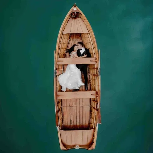 Romantisches Brautpaar liegt eng umschlungen in einem Holzboot auf türkisgrünem Wasser – aufgenommen aus der Vogelperspektive.