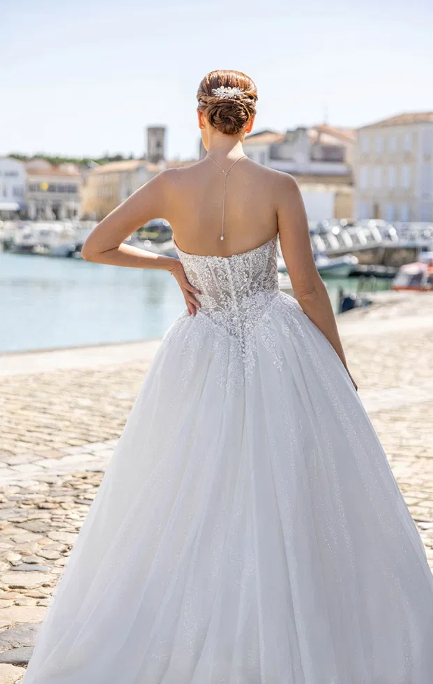 Rückenansicht eines Prinzessinnen-Brautkleides mit besticktem Corsagenoberteil, funkelndem Tüllrock und zarter Schleppe, aufgenommen an einer Hafenpromenade.
