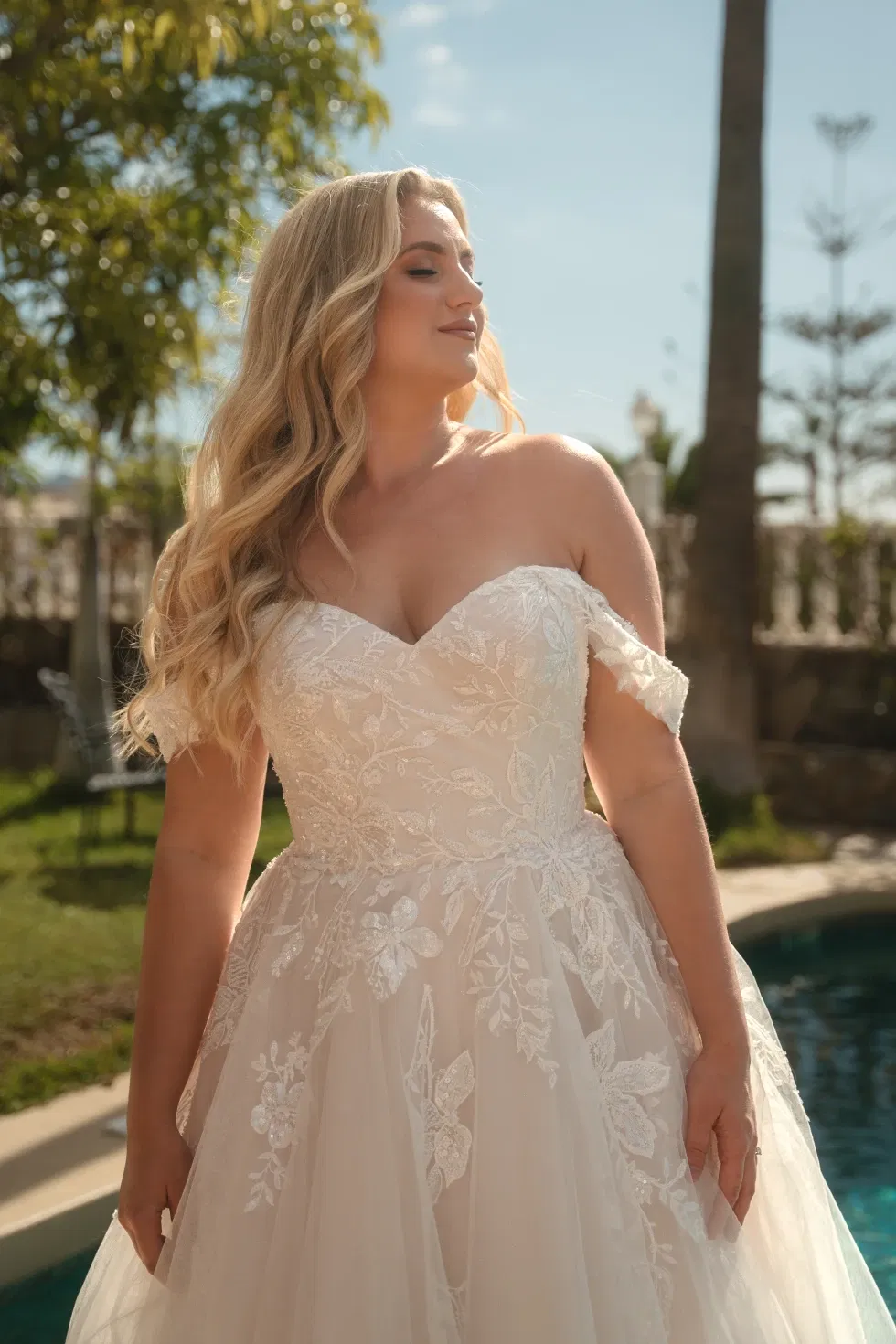 Curvy Bride in einem romantischen Off-Shoulder-Brautkleid mit feiner Spitze und Tüllrock aus der Madonna-Kollektion von Diane Legrand.