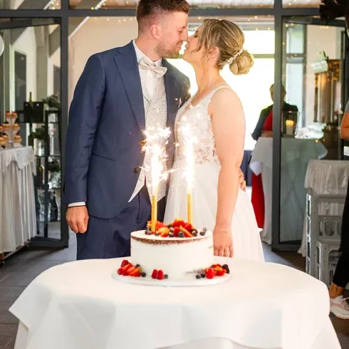 Ein Hochzeitspaar steht hinter einer weißen Torte verziert mit Beeren
