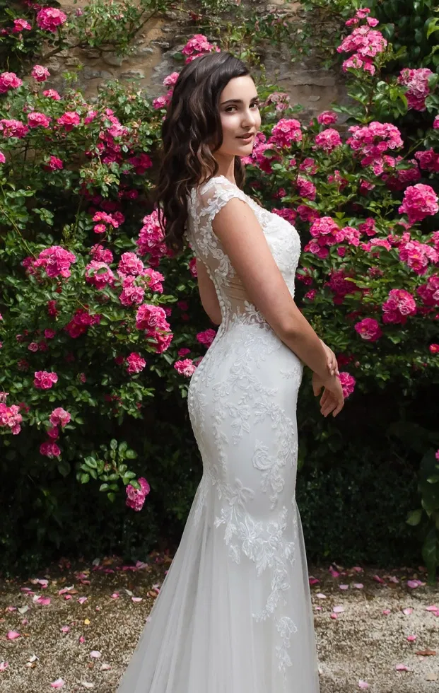 Seitenansicht einer Braut in einem sinnlichen Anna-Isadora-Brautkleid im Fit-and-Flare-Stil mit floraler Spitze und transparenter Rückenpartie, inszeniert im Rosengarten.