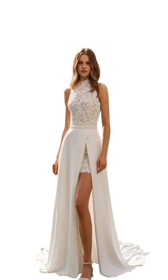 Brautmodell trägt ein modernes Brautkleid mit hochgeschlossenem Spitzenoberteil, kurzem Spitzenrock und fließendem Überrock mit hohem Schlitz, klar inszeniert vor weißem Hintergrund.