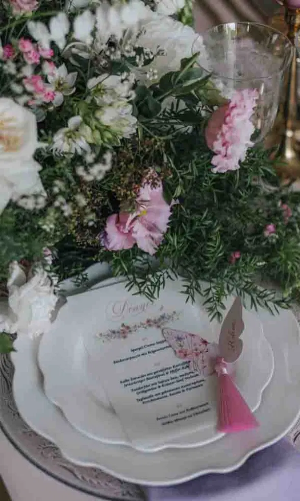 Festlich gedeckter Hochzeitstisch mit floraler Menükarte auf weißen Tellern, umgeben von üppigen rosa-weißen Blüten.