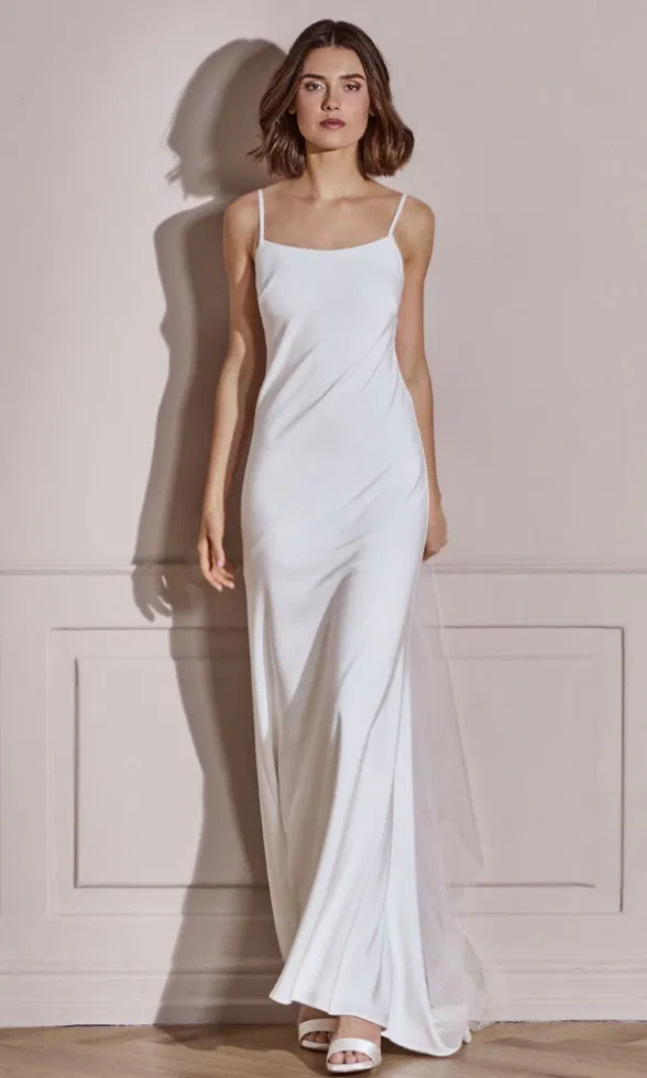 Schlankes Spaghettiträger-Brautkleid mit fließender Silhouette, aufgenommen in hellem Innenraum.