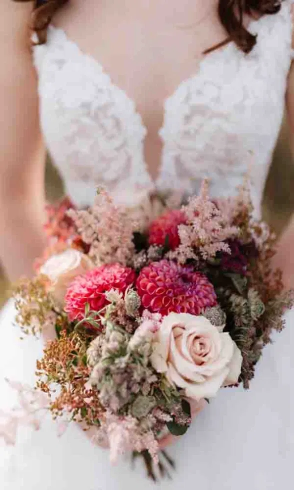 Nahaufnahme eines romantischen Brautstraußes mit Rosen, Dahlien und zarten Trockenblumen in Rosa- und Beerentönen.