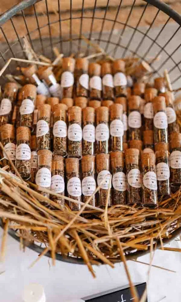 Detailaufnahme eines Korbs voller kleiner Glasfläschchen mit Korken und liebevollen Labels, die als Gastgeschenke dienen.