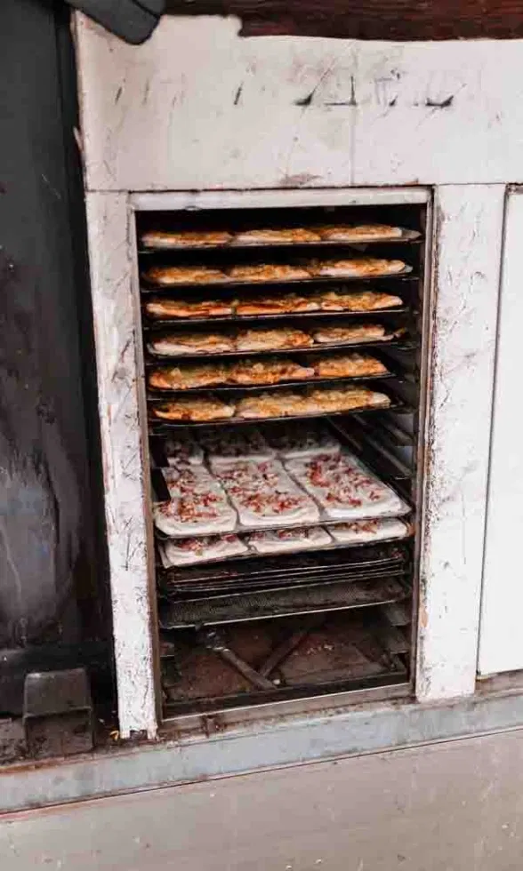 Ein geöffneter Ofen voller frisch belegter und gebackener Flammkuchen in verschiedenen Backstufen.