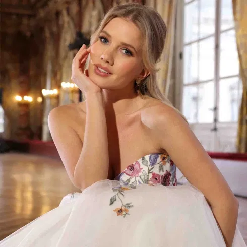 Braut im bestickten Kleid mit floralen Details, die sanft in die Kamera lächelt.