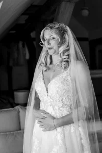 Emotionale Braut mit Schleier und floraler Spitze hält inne und genießt einen besonderen Moment vor der Trauung.
