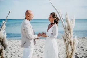 Brautpaar tauscht am Strand unter einem minimalistischen Traubogen die Ringe und genießt eine intime Trauung am Meer.