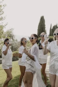 Braut feiert mit ihren Bridesmaids in Schlafanzügen und Herz-Sonnenbrillen ausgelassen beim Getting Ready im Garten.