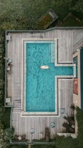 Luftaufnahme einer Braut im weißen Kleid, die entspannt in einem rechteckigen Pool treibt.