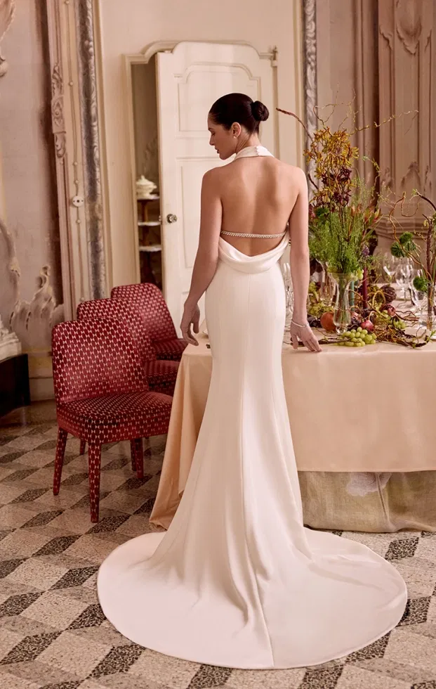 Elegantes Brautkleid mit tiefem Rückenausschnitt, drapiertem Stoff und langer Schleppe in einem historischen Raum